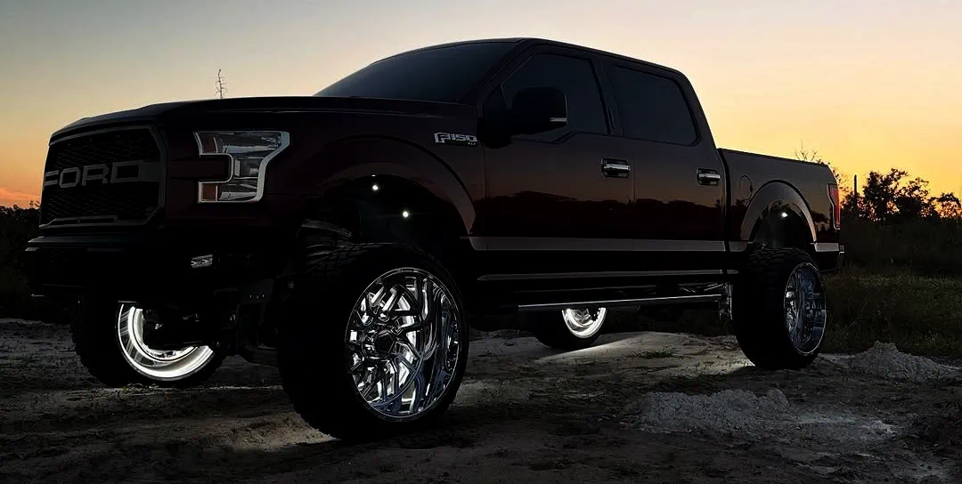 Lifted Ford F-150 truck equipped with single color rock lights illuminating the ground during sunset off-road